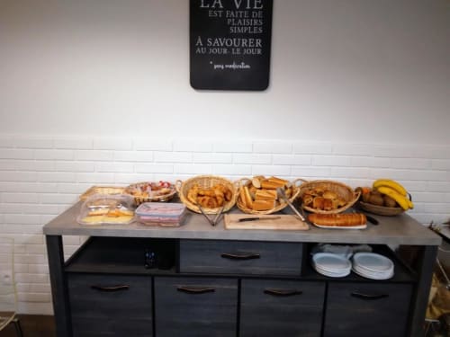 Buffet du petit-déjeuner à l'Hôtel le Vauban à Carentan : viennoiseries, pains frais et fruits sur comptoir foncé.