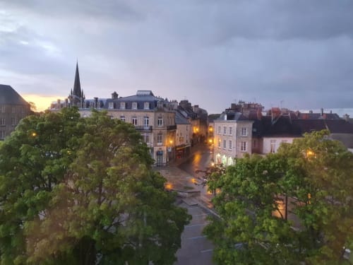 L'Hôtel le Vauban à Carentan au crépuscule, bâtiments historiques illuminés et place ombragée