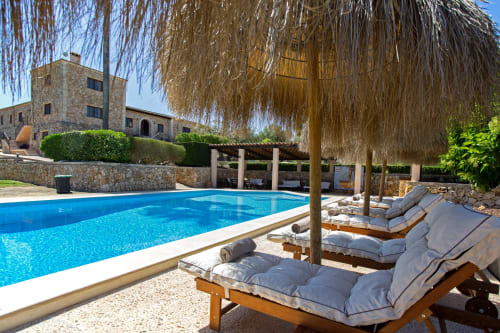 Área de piscina de lujo en Agroturismo Ses Illes en Costitx con tumbonas, pérgola y villa de piedra