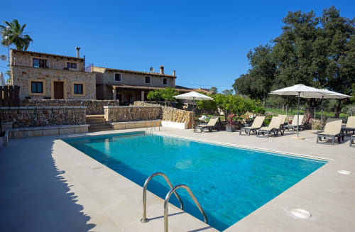 Área de piscina de Agroturismo Ses Illes en Costitx con tumbonas, sombrillas y villa de piedra rústica