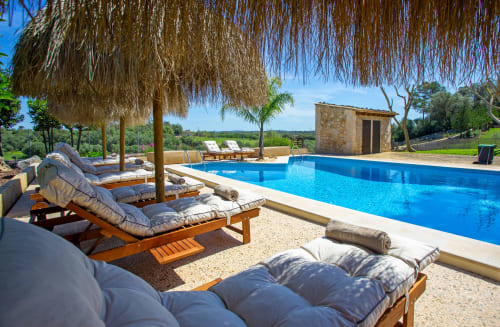 Luxueux espace piscine à Agroturismo Ses Illes à Costitx avec transats, parasol chaumé et vue sur la campagne