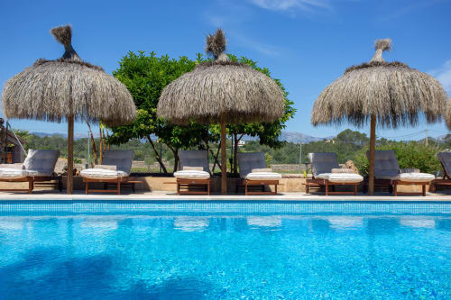 Zone de piscine luxe à l'Agroturismo Ses Illes à Costitx avec parasols en chaume et transats vue sur la campagne