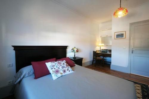 Quarto luminoso com cabeceira preta, almofadas vermelhas, roupa de cama floral, luminária pendente, área de trabalho e pisos de madeira em Santiago