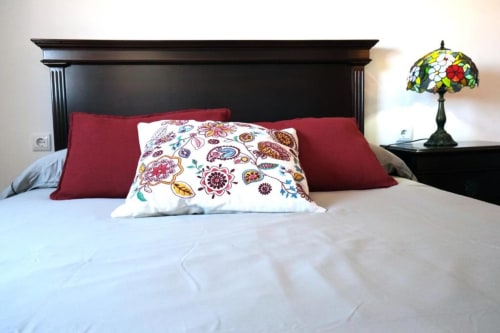 Quarto da Santiago de Caminha Boutique Hostel com cabeceira preta, almofadas bordô, roupa de cama floral e luminária Tiffany.