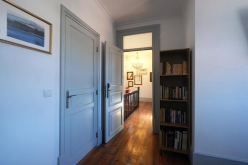 Corredor do Santiago de Caminha Boutique Hostel com portas azuis, pisos de madeira, estante de livros e acesso à vista do jardim