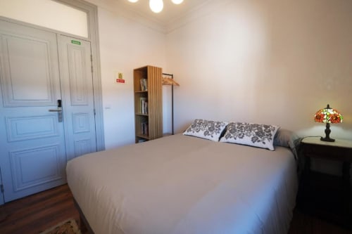Quarto luminoso na Pousada Boutique Santiago de Caminha em Portugal com cama de casal, prateleiras em madeira e luminária decorativa