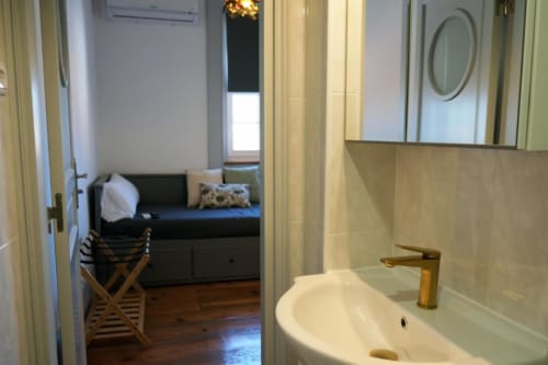 Banheiro moderno com pia branca e torneira dourada; vista do quarto com cama preta na pousada Santiago de Caminha