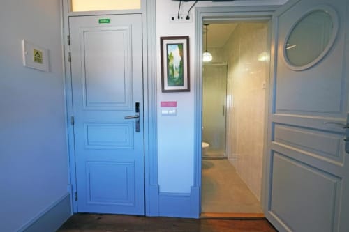 Corredor de albergue com portas azuis, placa de saída, quadros na parede e acesso aos quartos no Santiago de Caminha Boutique Hostel em