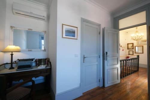 Corredor do Santiago de Caminha Boutique Hostel com portas azuis, pisos de madeira, escrivaninha com luminária e acesso à escada
