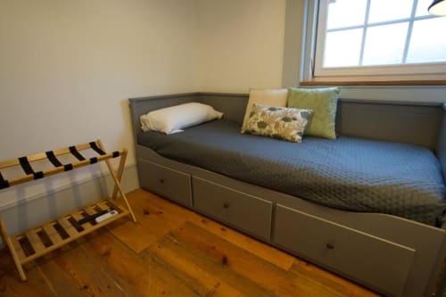 Quarto moderno na pousada de Caminha com cama cinza, travesseiros brancos, almofadas amarelo-esverdeadas, suporte de malas em madeira e piso de madeira maciça.