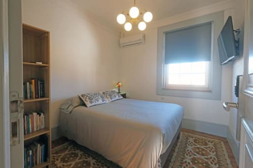 Quarto luminoso da Santiago de Caminha Boutique Hostel com cama de casal, prateleiras de madeira, luminária suspensa e janela com persiana azul