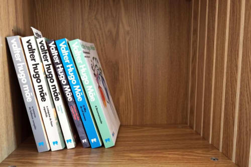 Pilha de livros coloridos de Valter Hugo Mãe na prateleira de madeira no Quarto 202 da Pousada Boutique Santiago de Caminha