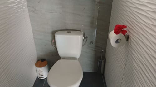 Salle de bains immaculée avec toilettes blanches et murs carrelés texturés à la Résidence KaZa Lou-Lou en Guadeloupe