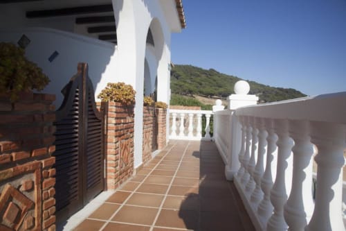 Luminosa terraza del Hostal Mar de Frente en Los Caños de Meca con barandillas blancas, piso de baldosa roja y vistas a la sierra