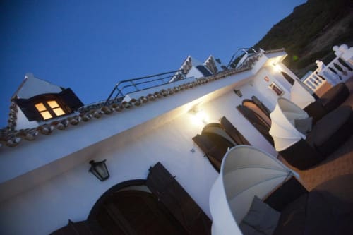Hostal encalado con ventanas iluminadas al atardecer en Los Caños de Meca, España