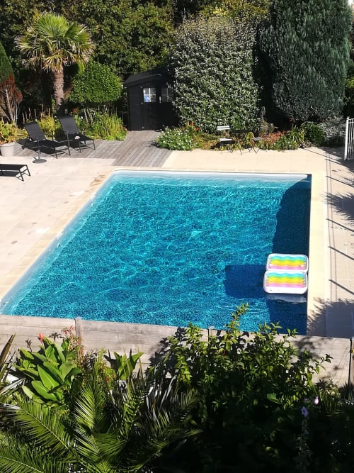 Türkisblauer Pool in den Villas Du Bord De Mer in Guidel mit Liegen, tropischem Garten und schwarzer Villa am Wasser