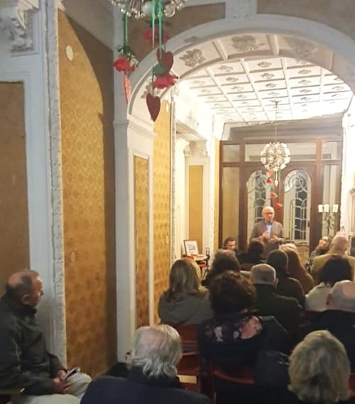 Invités réunis dans l'élégant couloir du Palazzo Losio aux plafonds voûtés, décorations festives, un homme s'adressant au groupe