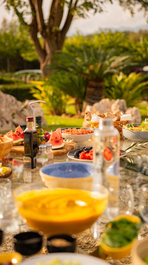 Table de repas en plein air à Agroturismo Ses Illes avec bols colorés, fruits frais et vue sur la campagne méditerranéenne