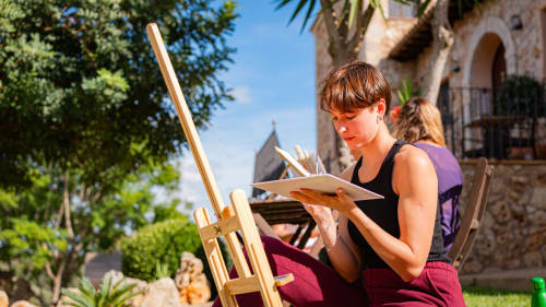 Un client peint en plein air à l'Agroturismo Ses Illes à Costitx, Espagne, avec un bâtiment en pierre historique et des jardins luxuriants