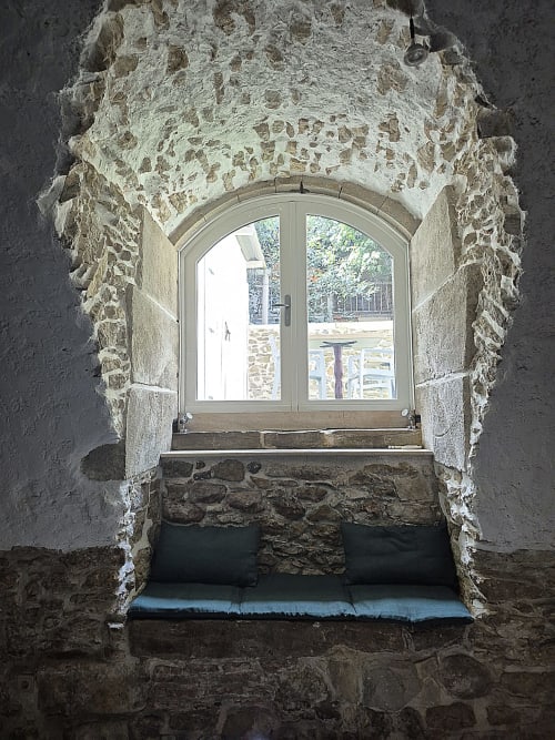 Fenêtre en pierre médiévale à arc dans la salle de réception des Remparts de Mirepoix, vue sur le jardin
