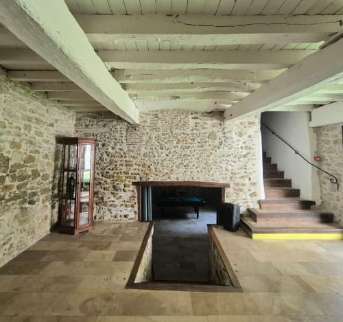 Hall d'accueil rustique aux murs en pierre avec poutres apparentes et escalier en bois aux Remparts de Mirepoix