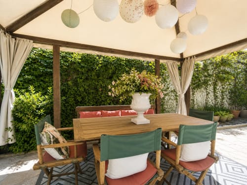 Pergola Viento de Ladera avec table de salle à manger en bois, chaises vertes, murs couverts de lierre et lanternes en papier blanc