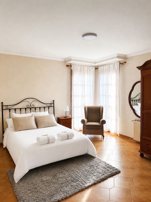 Elegante dormitorio en Casa Rural Finca El Olivar con cama de hierro forjado, paredes beige, suelos de madera y cortinas translúcidas en Las