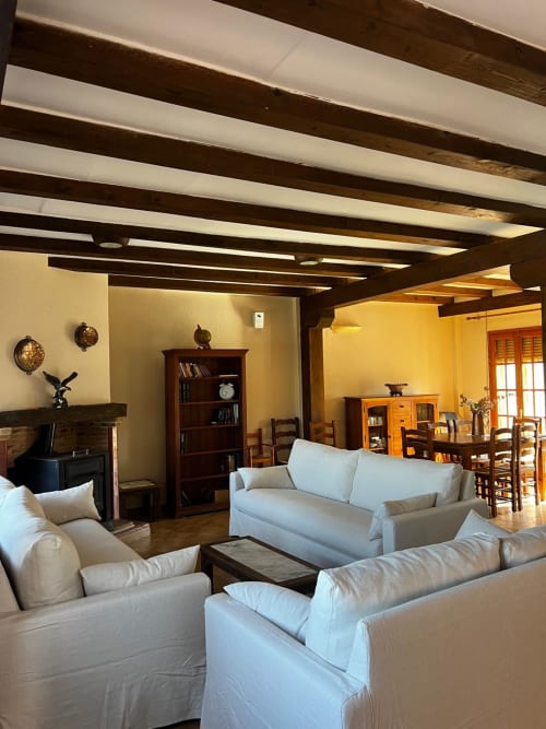 Amplio salón en Casa Rural Finca El Olivar con sofás crema, vigas de madera vista, chimenea y comedor