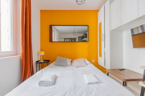 Chambre d'hôte moderne à Mattbnb Metz avec mur d'accent orange vif, lit queen-size, bureau et miroir encadré