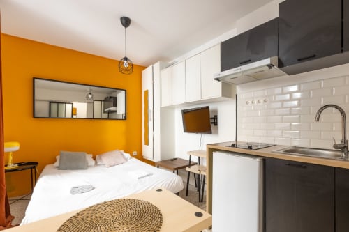 Studio à Metz avec mur d'accent orange, lit, kitchenette aux armoires blanches et équipements modernes