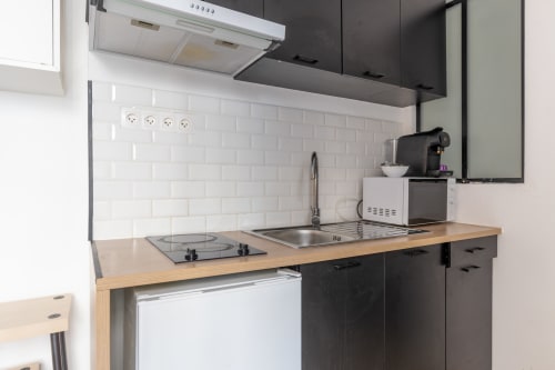 Petite cuisine moderne dans un studio à Metz : meubles noirs, plan de travail en bois et carrelage blanc en métro