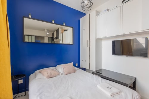 Chambre studio moderne à Metz avec mur d'accent bleu, lit blanc, TV écran plat et mobilier contemporain chez Mattbnb