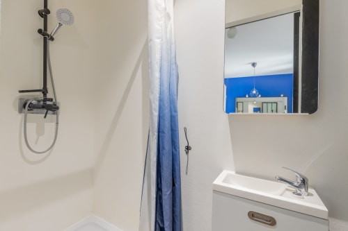 Salle de bain moderne du Studio 201 Mattbnb à Metz, avec douche, lavabo, miroir et mur d'accent bleu