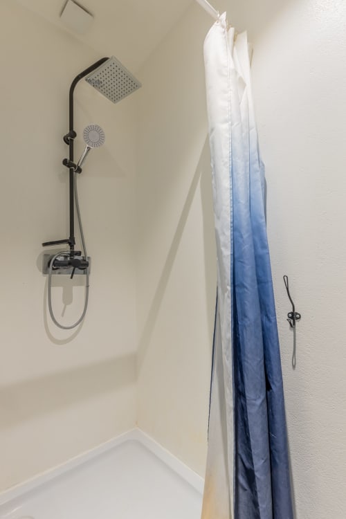 Douche moderne du studio Mattbnb 201 à Metz avec pommeau de douche pluie noir et douchette, porte-serviettes blanc et bleu