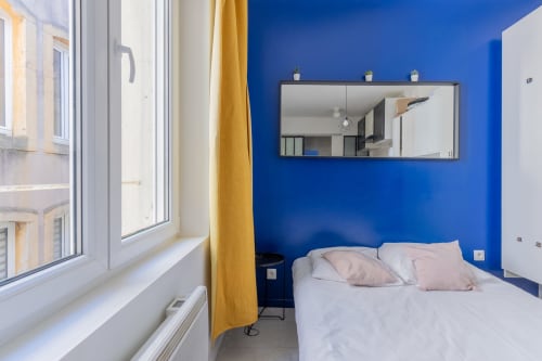 Chambre moderne à Metz aux murs bleu vif, lit blanc, grande fenêtre et miroir mural