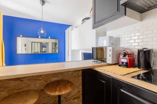 Cuisine moderne du studio à Metz avec mur d'accent bleu, comptoir en bois, électroménagers noirs et luminaires suspendus