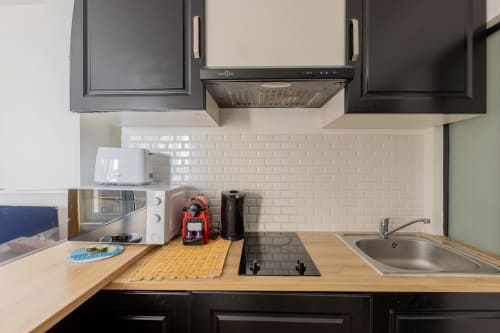 Cuisine moderne dans un appartement messin avec armoires noires, plan de travail en bois, cuisinière et carrelage métro blanc