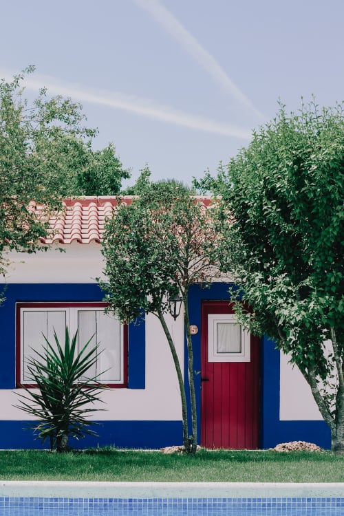 Charmosa casarão azul e branco em Herdade da Cova da Onça com porta vermelha, persianas verdes e paredes cobertas de hera