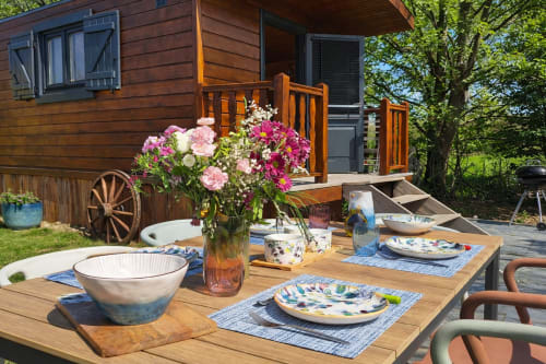 Espace de repas en plein air à Roulotte Gîtes O Bien être à Porspoder avec fleurs, vaisselle et chalet en bois