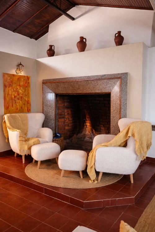Sala de estar aconchegante com poltronas creme, lareira e vasos de terracota na Herdade da Cova da Onça, Portugal
