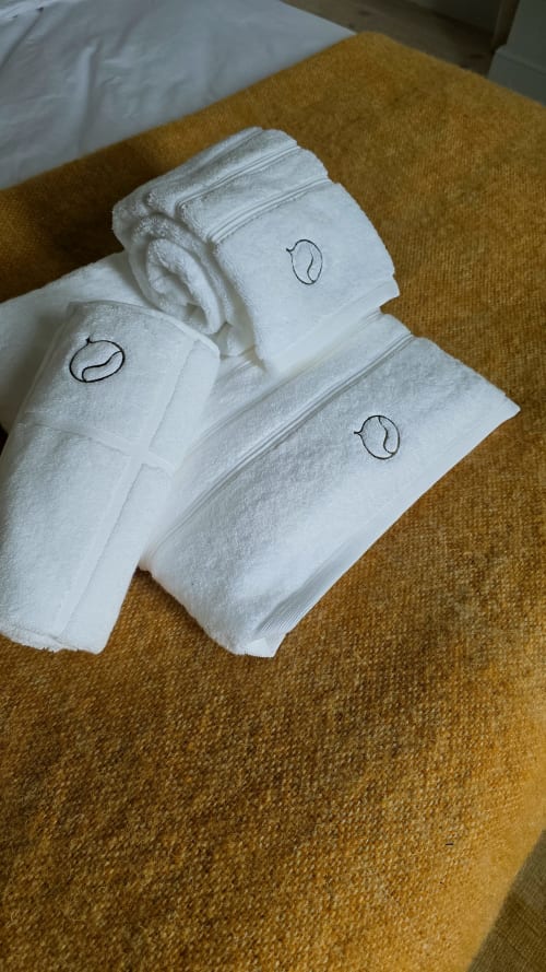 Rolled white towels with embroidered logo on mustard bedspread in Marie-Christine Suite at Castanea Business & Suites,