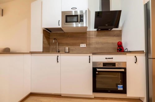 Moderna kitchenette del apartamento La Dormilona, Gestyp-AT Mérida con muebles blancos, encimera de madera y acero inoxidable
