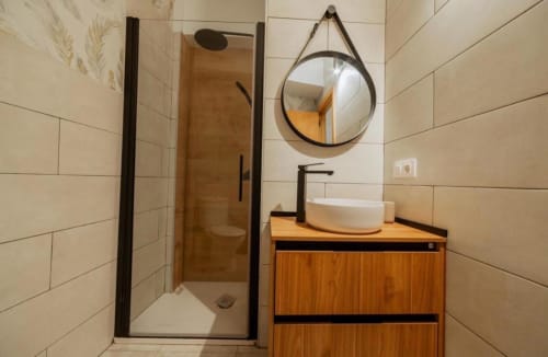 Baño moderno en apartamento La Dormilona de Gestyp-AT Mérida con paredes alicatadas, tocador de madera, espejo redondo y ducha de acceso directo