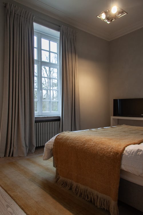 Marie-Christine Suite bedroom at Castanea Business & Suites in Merelbeke with garden view, bed with caramel throw, curtains,