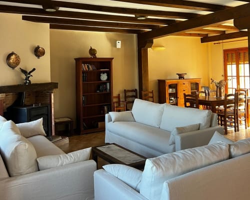 Spacious living room at Casa Rural Finca El Olivar with cream sofas, dark wood beams, fireplace, and rustic decor