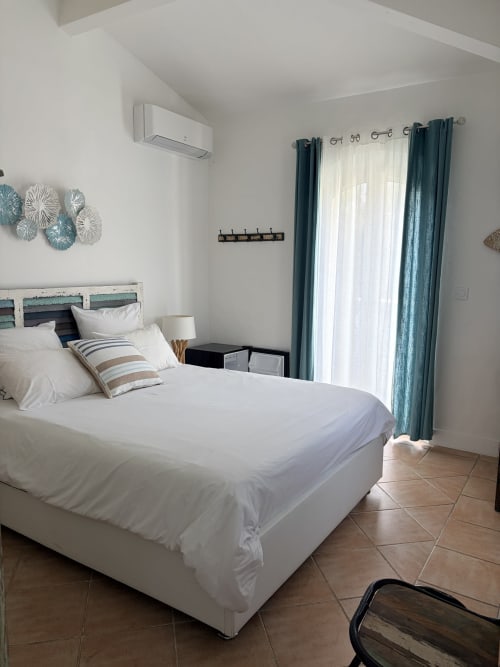 Helles Schlafzimmer in La Parenthèse de Villepey mit weißer Bettwäsche, türkisfarbenen Gardinen und Gartenblick in Saint-Aygulf