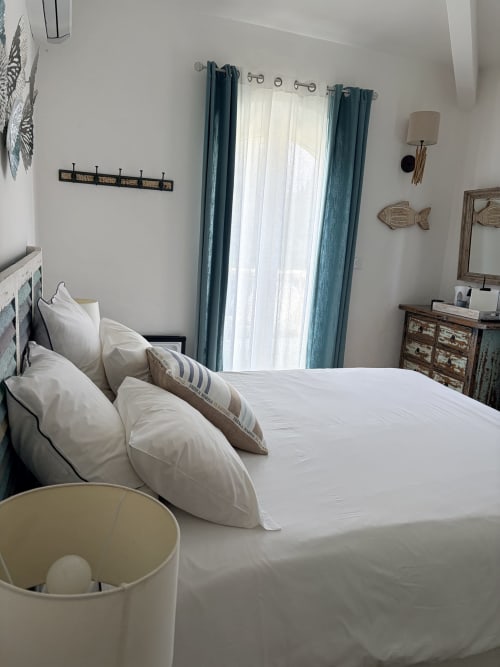 Helles Schlafzimmer in La Parenthèse de Villepey mit weißer Bettwäsche, türkisfarbenen Vorhängen und Gartenblick in Saint-Aygulf