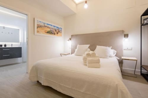 Habitación moderna en Calma Places, Sevilla con cama blanca, cabecera beige, cocina y baño
