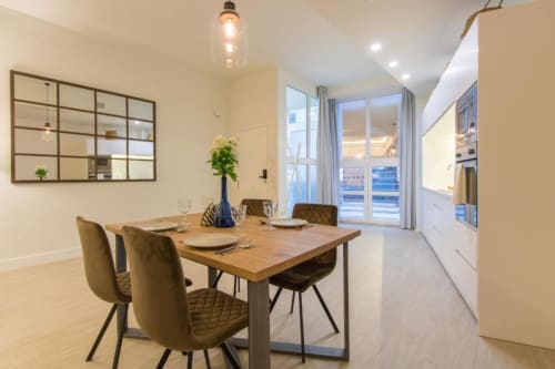 Zona de comedor del apartamento Almirante Hoyos en Calma Places Sevilla con mesa de madera, sillas de oliva y vistas a la ciudad