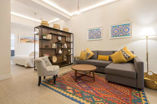 Sala de estar moderna en Calma Places Sevilla con sofá gris, cojines amarillos, mesa de café de madera y alfombra marroquí decorativa